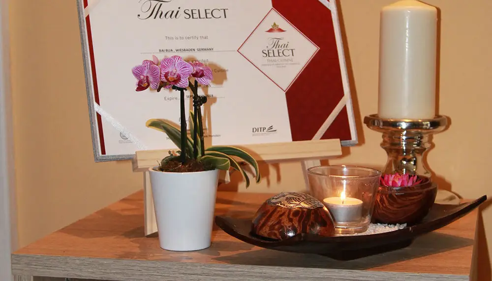 Die Thai-SELECT-Urkunde im Bai Bua, daneben Orchidee und Kerze